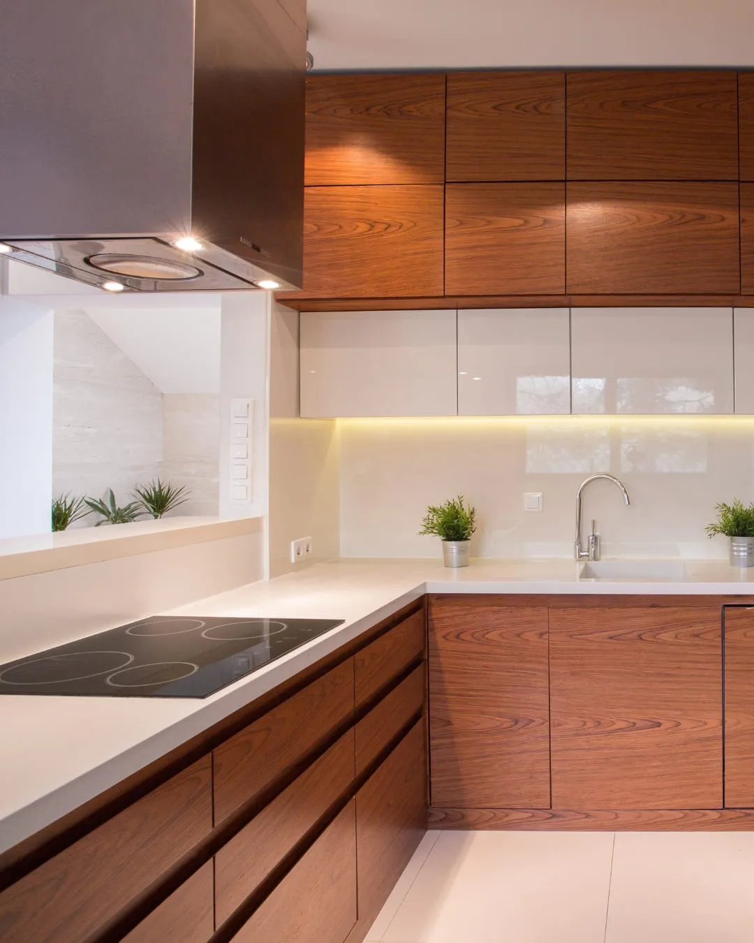 Modern kitchen with wooden cabinets, white countertops, and stainless steel faucet. Induction cooktop on left, small potted plants decorate.