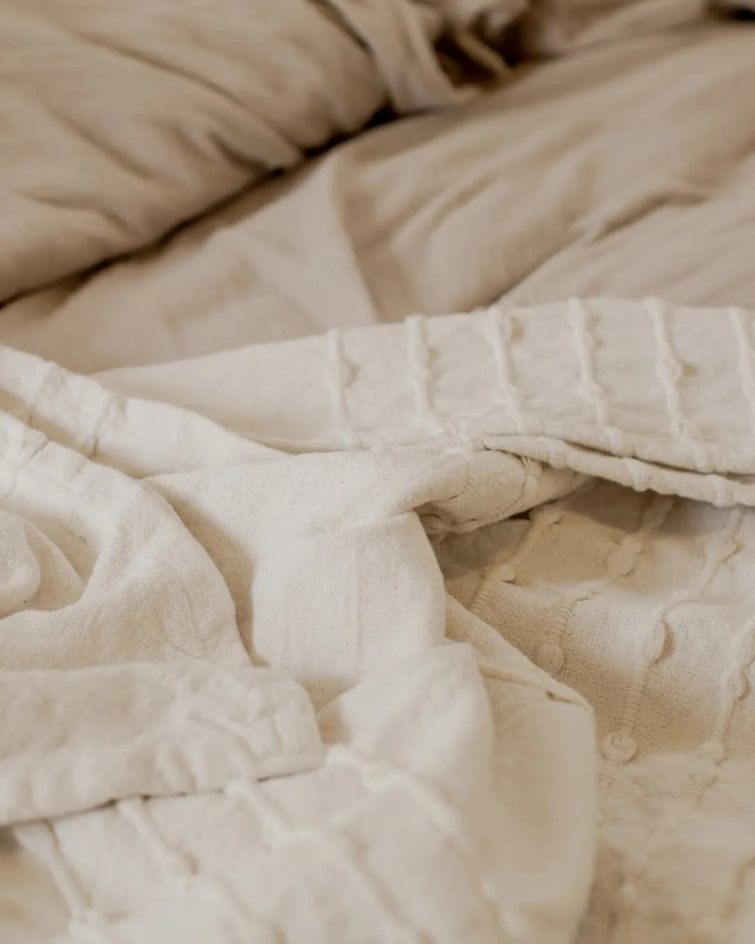 Cream-colored textured bedding is softly rumpled, creating a cozy and relaxed atmosphere. No text is visible.