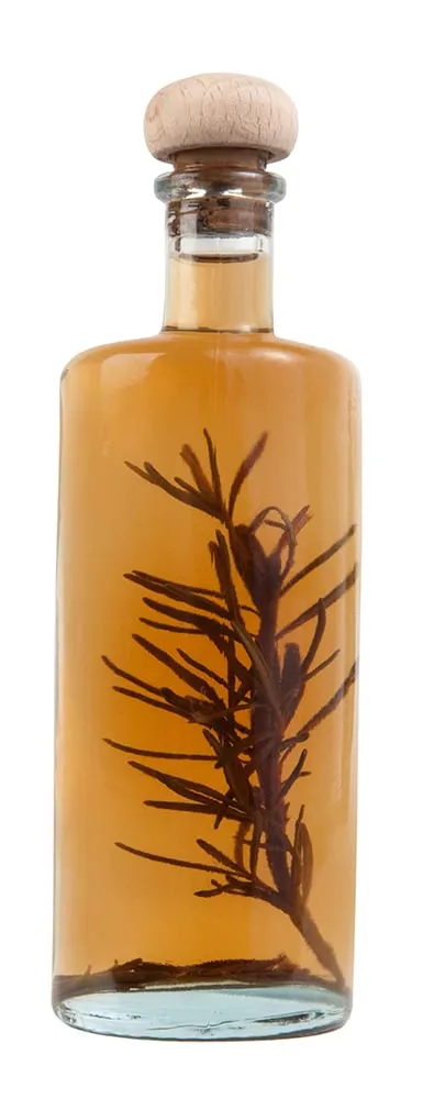 A clear bottle with a wooden cork, containing amber liquid and a sprig of rosemary, isolated on a white background.