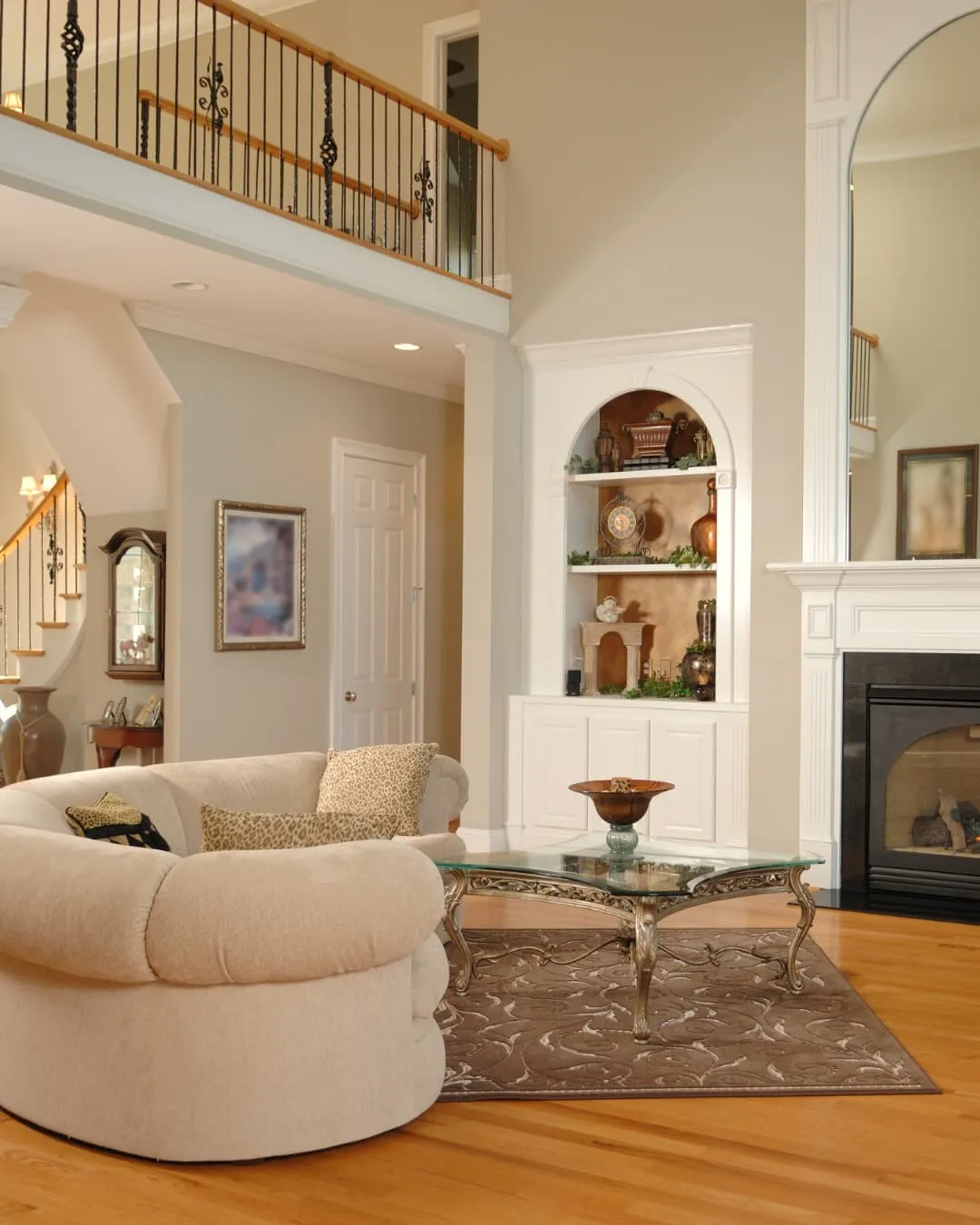 Elegant living room with beige sofa, patterned pillows, glass coffee table, decorative shelves, and fireplace. Warm, inviting ambiance.