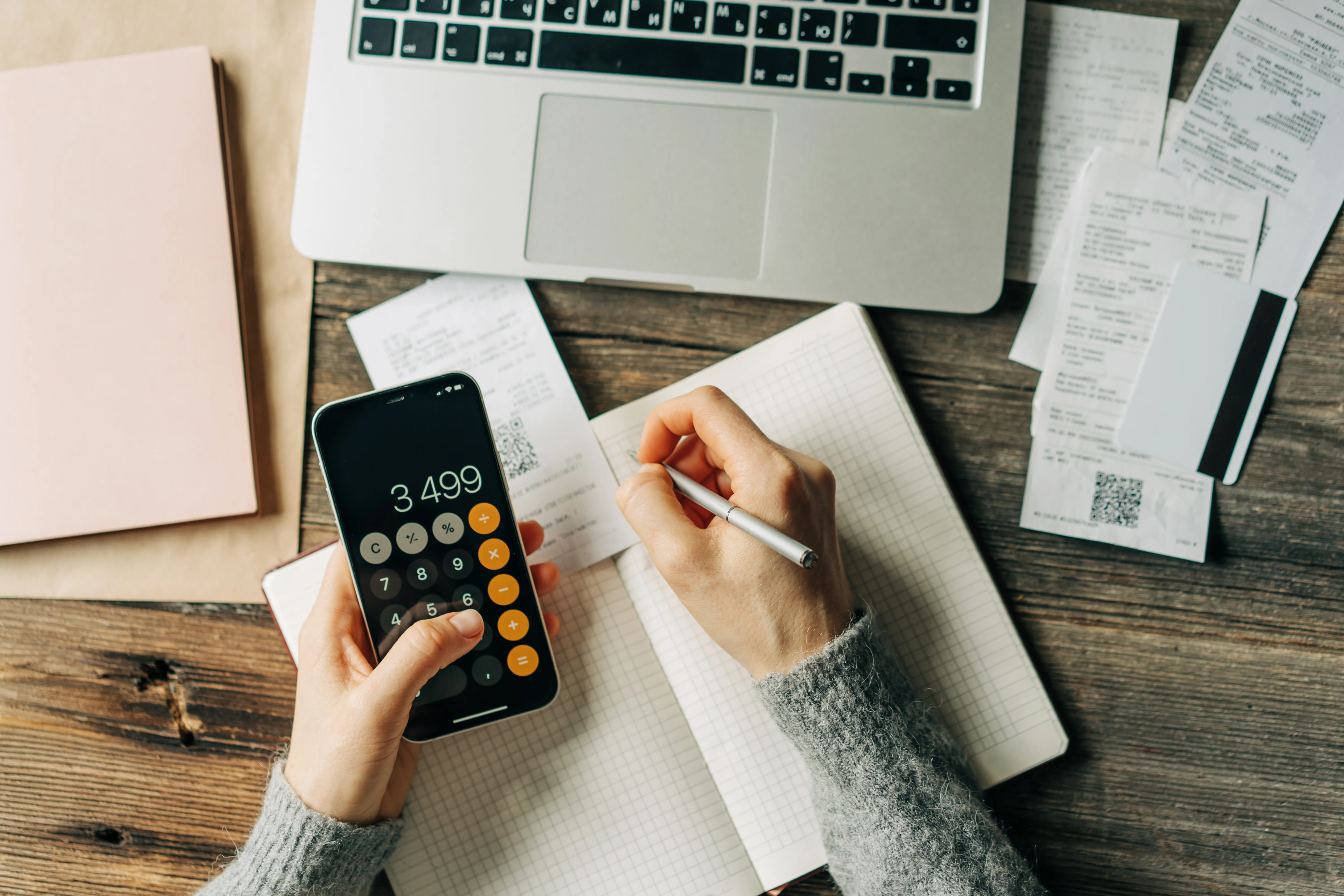 A work desk seen from above with a calculator, notebook, and paperwork for budgeting.