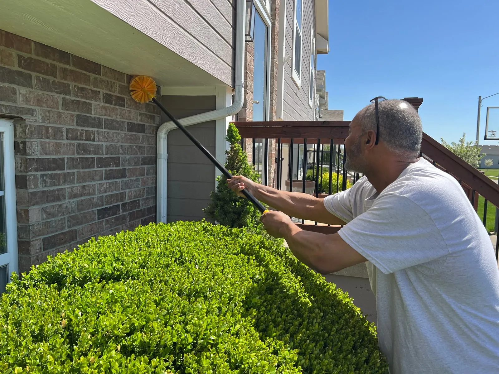 Using the de-webbing brush on an extension pole to clear webs from the eaves of a home.