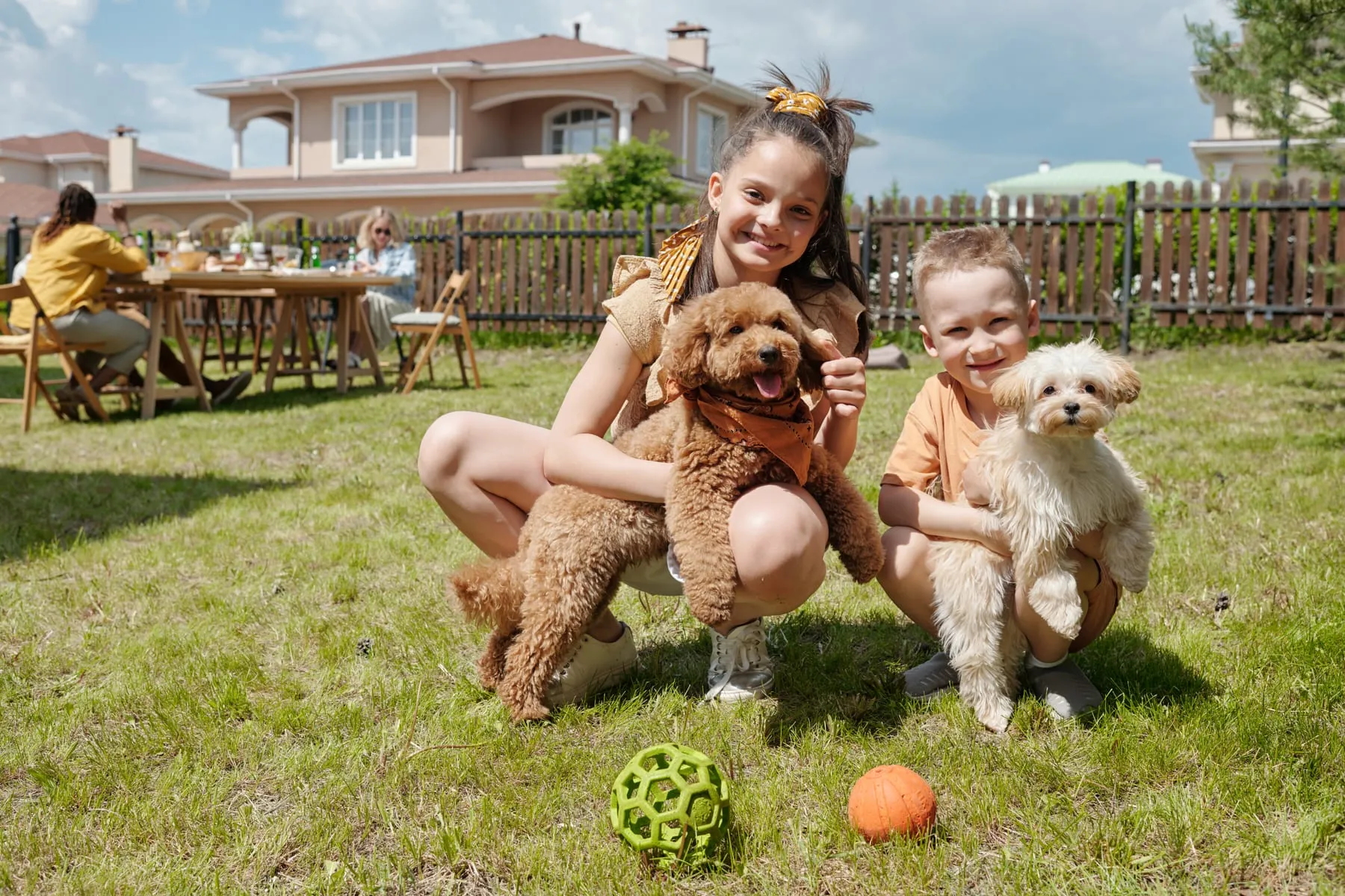 Two children in a sunny backyard, each holding their small dog.